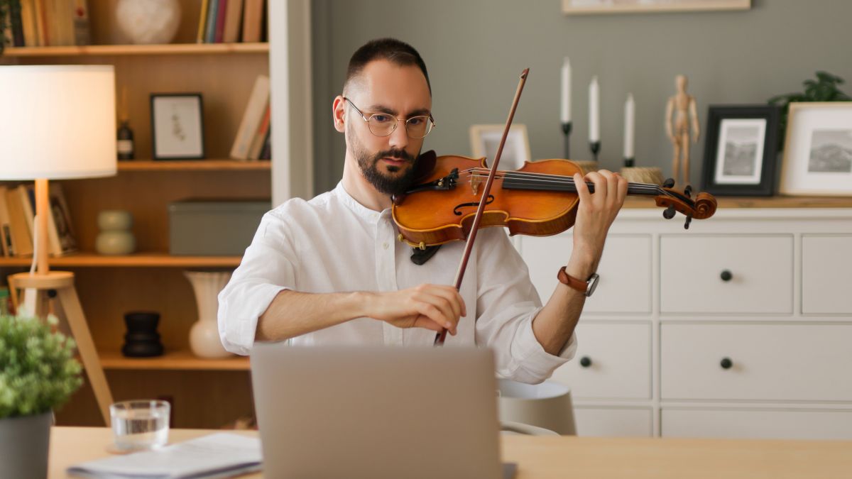 Adult male taking online violin lessons playing on his laptop